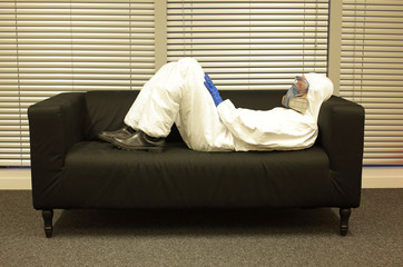 Quarantine - home arrest. Professional in protective uniform and mask, lying on the sofa, waiting ...