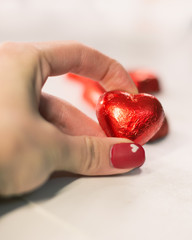 Girl hand holding red heart shaped candy. Red valentine's day manicure. Shallow depth of field, soft focus and blur