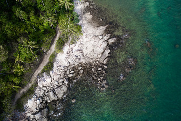 Aerial drone view of rocky shore with turquoise sea water and tropical green trees