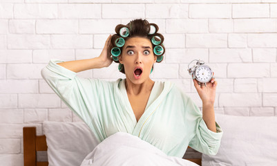 Shocked Woman Holding Clock Being Late Sitting In Bed Indoors