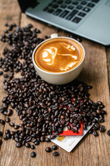 Hot latte art coffee with laptop on wood table