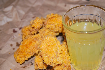 Breaded chicken wings and a glass of lemonade on a grey paper background. Close up.