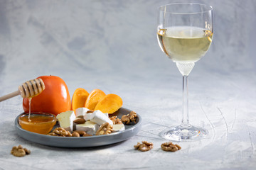 Brie cheese and persimmon with almonds and walnuts on a plate and a grey background. Glass of dry white wine