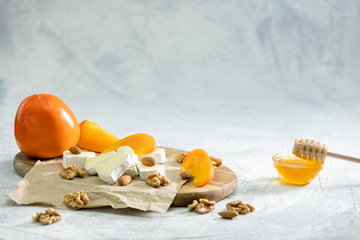 Brie and persimmon with almonds and walnuts on a wooden Board and a gray background. Honey in a glass bowl.Space for text