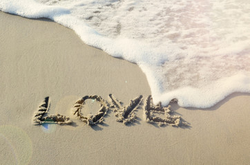 Word Love written in sand on the beach with wave and sun. Holidays and travel in summer time.