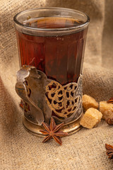 A glass of tea in a vintage Cup holder, stars of star anise and pieces of brown sugar on a background of rough homespun fabric. Close up.