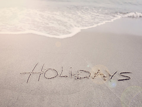 Holidays handwritten on sandy beach with soft wave  sun and copy space