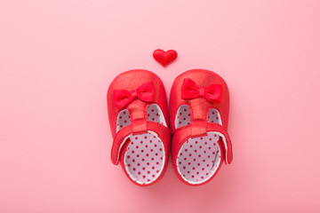 Bright red baby shoes with heart on light pink table background. Pastel color. Closeup. Top view.