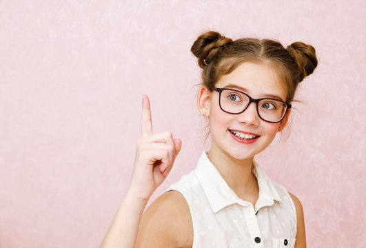 Portrait of funny smiling little girl child wearing glasses with finger up isolated on a pink background