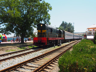 Fototapeta premium Locomotive with three cars going along the railway track laid along the waterfront of the seaside town , summer day.