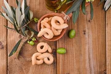 Taralli is a traditional Italian snack food typical of Puglia regional cuisine. Tarallini with fresh olive branches on a wooden table. Copy space. Above