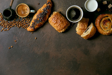 Variety of traditional french puff pastry raisin and chocolate buns, croissant with various cups of coffee and milk, cezve, recycled wooden spoon of sugar over dark texture background. Flat lay, space
