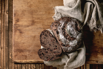 Sliced fresh baked artisan round homemade chocolate and cranberries rye bread on linen cloth over wooden table background. Flat lay, space