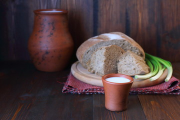 A clay cup of milk and loaf of bread on a wooden background.