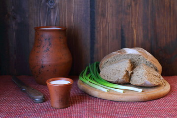 A clay cup of milk and loaf of bread on a wooden background.