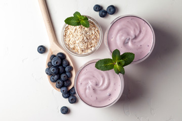 homemade blueberry yogurt with cereals and berries on a white table, two glasses of dairy product, ingredients for cooking