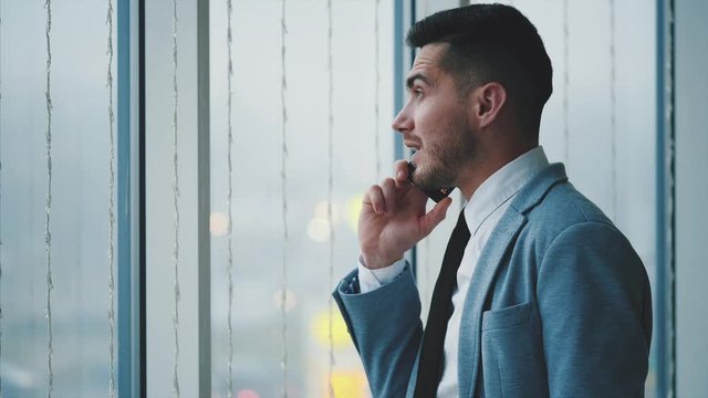 Business man is standing near the window. Man is lon phone. He is isolated, on white blurred background. Copy space. 4K.