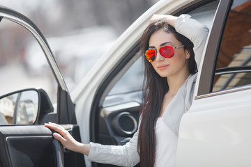 Stylish trendy woman in the car. Female driving an automobile. Attractive lady with flowers outdoors.
