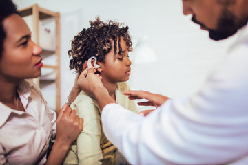 Smiling deaf girl with ear implant at doctor's office.