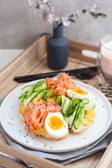 Smoked salmon, cream cheese and cucumber toast sandwiches with boiled egg on white plate.