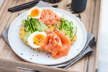 Smoked salmon, cream cheese and cucumber toast sandwiches with boiled egg on white plate.