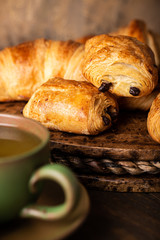 Freshly baked sweet buns puff pastry with chocolate and croissants on old wooden background. Breakfast or brunch concept