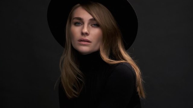 Portrait of a beautiful young blonde woman in a black hat with fields and a sweater. Romantic retro fashion image. A sensual emotional woman.