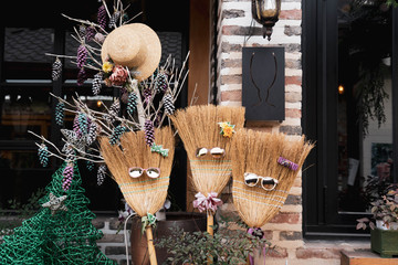 Decorative broom sticks wearing a sunglasses and flowers head pin. Summer fedora sun hat hanging on a tree branches.