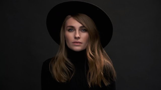 Portrait of a beautiful young blonde woman in a black hat with fields and a sweater. Romantic retro fashion image. A sensual emotional woman.