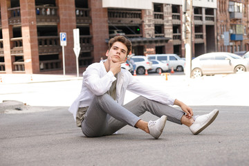 Fototapeta na wymiar guy model with a stylish haircut posing outdoors in a white shirt and gray trousers. trendy hairstyle rests near a modern business center. Attractive guy in the street on a summer day.