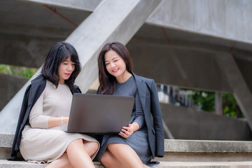 Two businesswoman working together with laptop in front of their office building