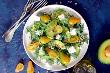 Avocado salad with yellow tomato, feta cheese, arugula and sunflower seeds. Top view with copy space. Healthy food.