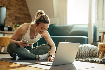 Happy sportswoman using laptop while relaxing on the floor at home.