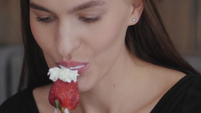 Big close up shot of young gorgeous fashionable woman in black blouse eating strawberry with a cream in loft city cafe slow motion