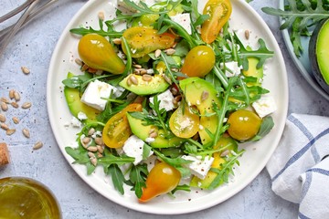 Avocado salad with yellow tomato, feta cheese, arugula and sunflower seeds. Top view with copy space. Healthy food.
