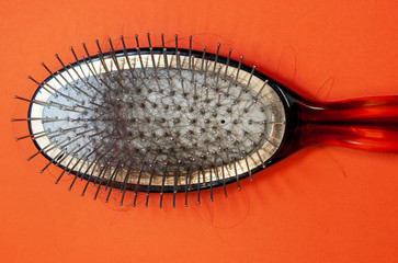 Old hairbrush with hair on an orange background close-up, top view