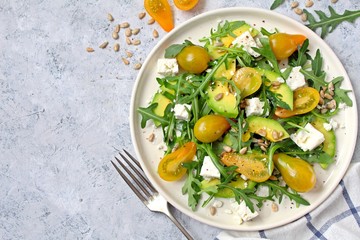 Avocado salad with yellow tomato, feta cheese, arugula and sunflower seeds. Top view with copy space. Healthy food.