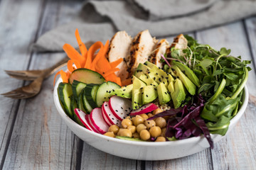 Close up view of a buddha bowl filled with grilled chicken and vegetables ready for eating.