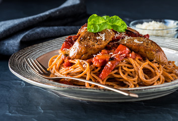 A close up of a plate of gourmet red pepper pasta topped with chorizo sausage, ready for eating.