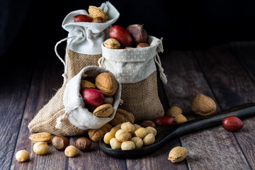 Close up of burlap sacks filled with assorted nuts in their shells with one sack tipped over, against a dark background. - Powered by Adobe