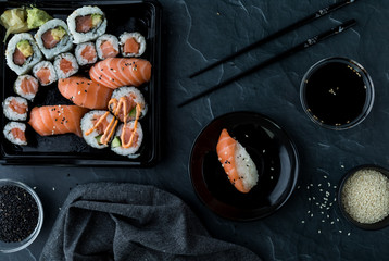 Top down view of assorted sushi along with sesame seeds, soy sauce and chopsticks.