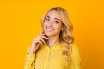 Cheerful girl touching chin and smiling, yellow background