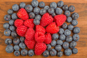raspberry heart in blueberry heap on wood background