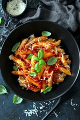 Penne pasta with tomato sauce, parmesan cheese and basil on dark background. Top view with copy space.