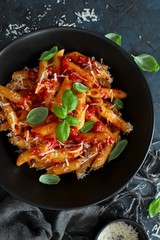 Penne pasta with tomato sauce, parmesan cheese and basil on dark background. Top view with copy space.