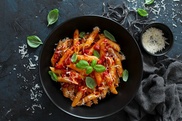 Penne pasta with tomato sauce, parmesan cheese and basil on dark background. Top view with copy space.