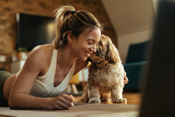 Happy athletic woman enjoying with her dog while exercising at home.