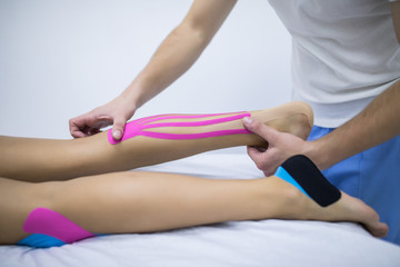 Obraz na płótnie Canvas Manual, physio and kinesio therapy techniques performed by a male physiotherapist on a training plastic spine and a female patient leg