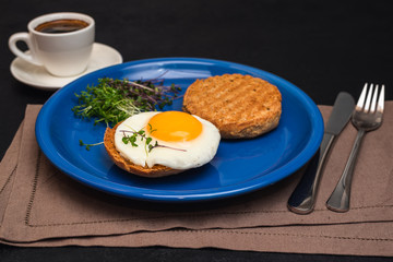 Fried egg, healthy whole wheat toast and microgreen on blue plate, cup of coffee for breakfast, brunch or lunch on dark background. Healthy eating concept. Close-up