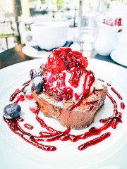 Delicious french toast with cheese cream, blueberries, cranberries and red fruits sauce on top served in white plate for sweet breakfast